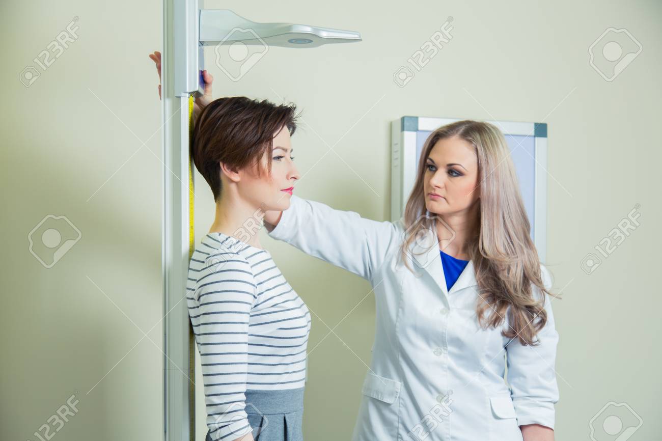 Doctor measures growth woman in medical office. - 56567494 Doctor measures growth woman in medical office. - 56567494