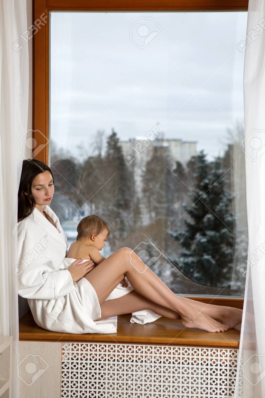 Mom With Little Son Sits On The Window In A Bathrobe After A Shower Stock Photo Mom With Little Son Sits On The Window In A Bathrobe After A Shower Stock Photo