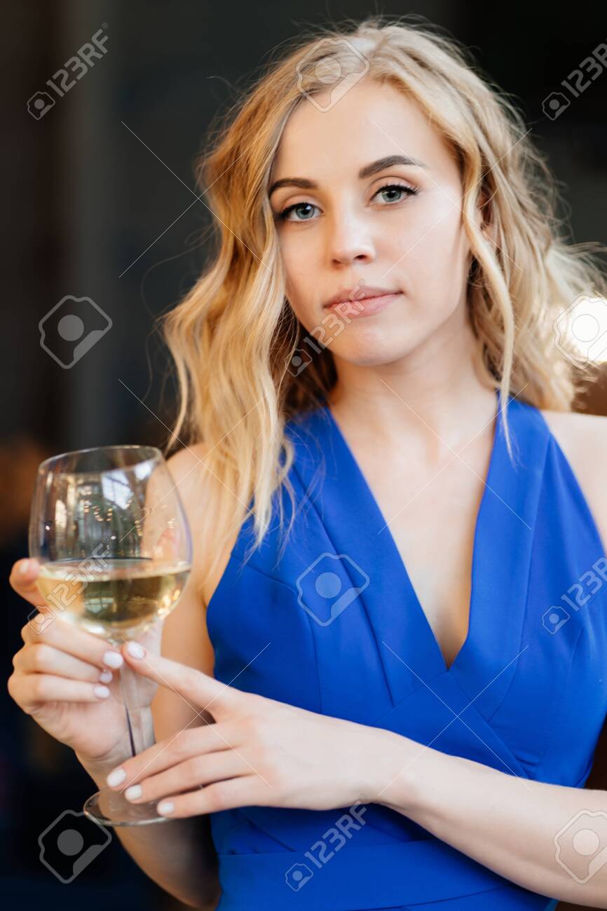 Beautiful Blonde Girl With Long Hair In A Blue Dress Standing With A Glass  Of Wine. A Romantic Dinner. Stock Photo, Picture and Royalty Free Image.  Image 151587153., image size:866x1300