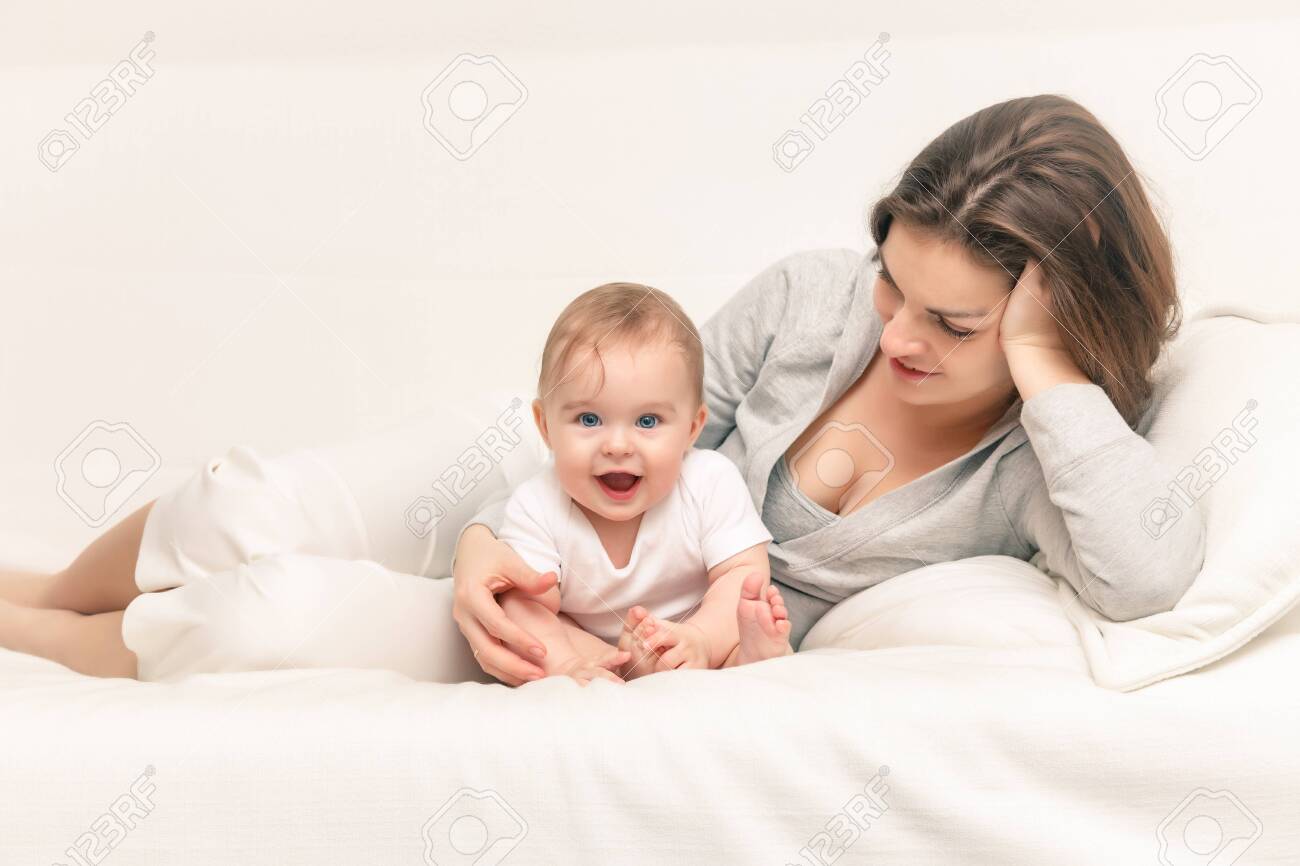 Happy mother playing with baby on white sofa - 148713567 Happy mother playing with baby on white sofa - 148713567