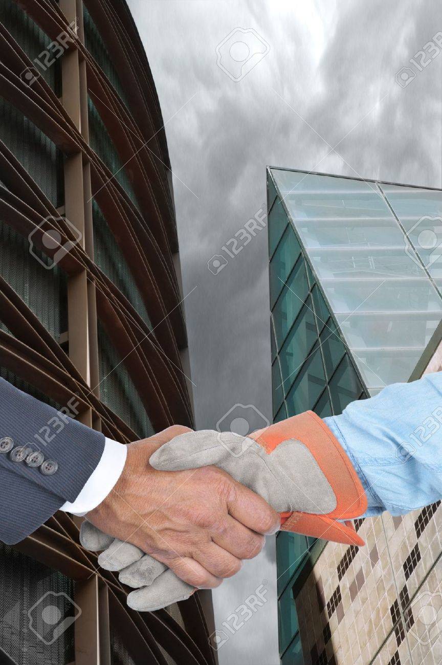 closeup of a manager and laborer shaking hands in front of two buildings manager