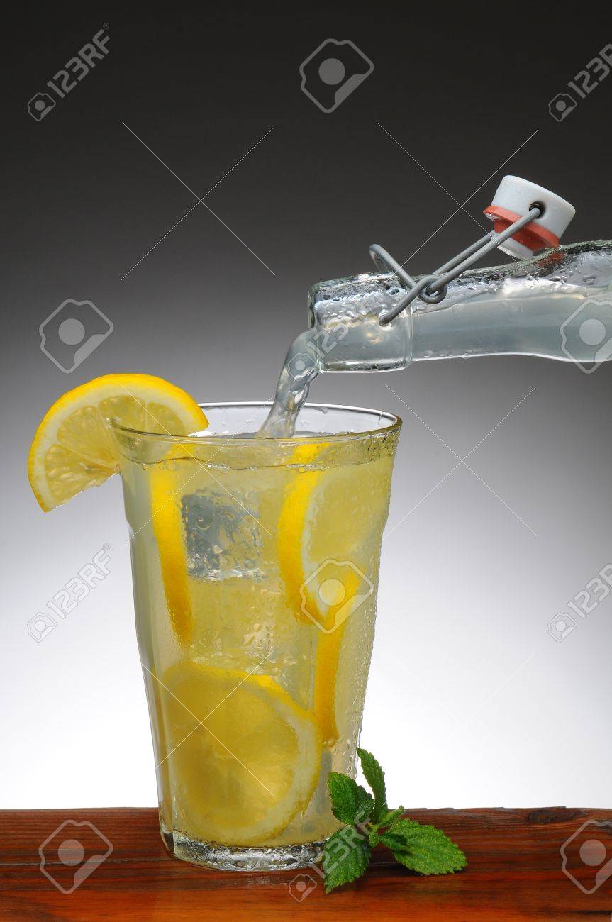 Lemonade Versando In Un Bicchiere Da Una Bottiglia Il Vetro è Su Un Rustico Tavolo Di Legno Con Una Luce Di Sfondo Grigio Scuro