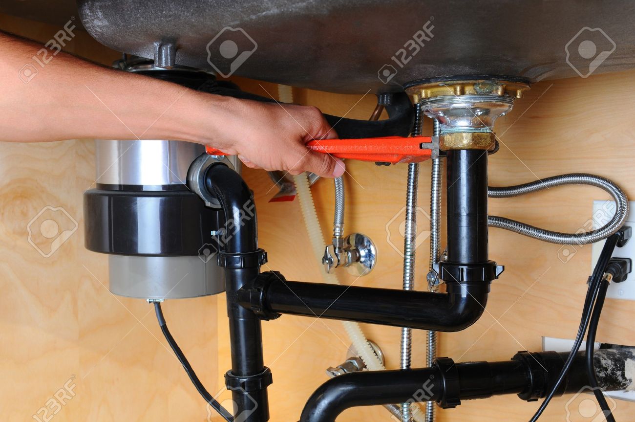 closeup of a plumber using a wrench to tighten a fitting beneath a kitchen sink only - Fitting Kitchen Sink closeup of a plumber using a wrench to tighten a fitting beneath a kitchen sink only - Fitting Kitchen Sink