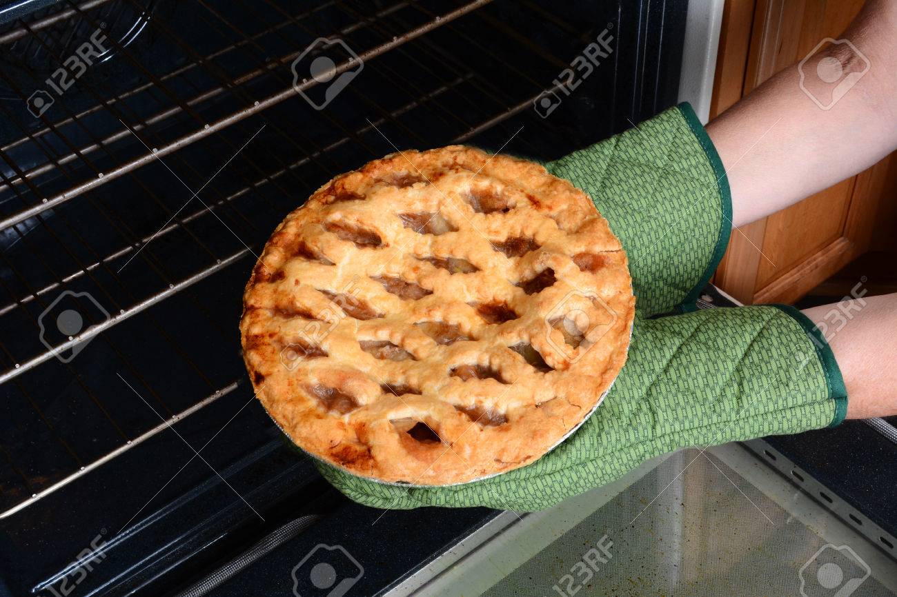 Closeup of a woman taking a fresh baked apple pie from the oven. Apple Pie is a traditional American dessert for Holiday feasts. Horizontal showing the womans hands in oven mitts only. - 33439032 Closeup of a woman taking a fresh baked apple pie from the oven. Apple Pie is a traditional American dessert for Holiday feasts. Horizontal showing the womans hands in oven mitts only. - 33439032