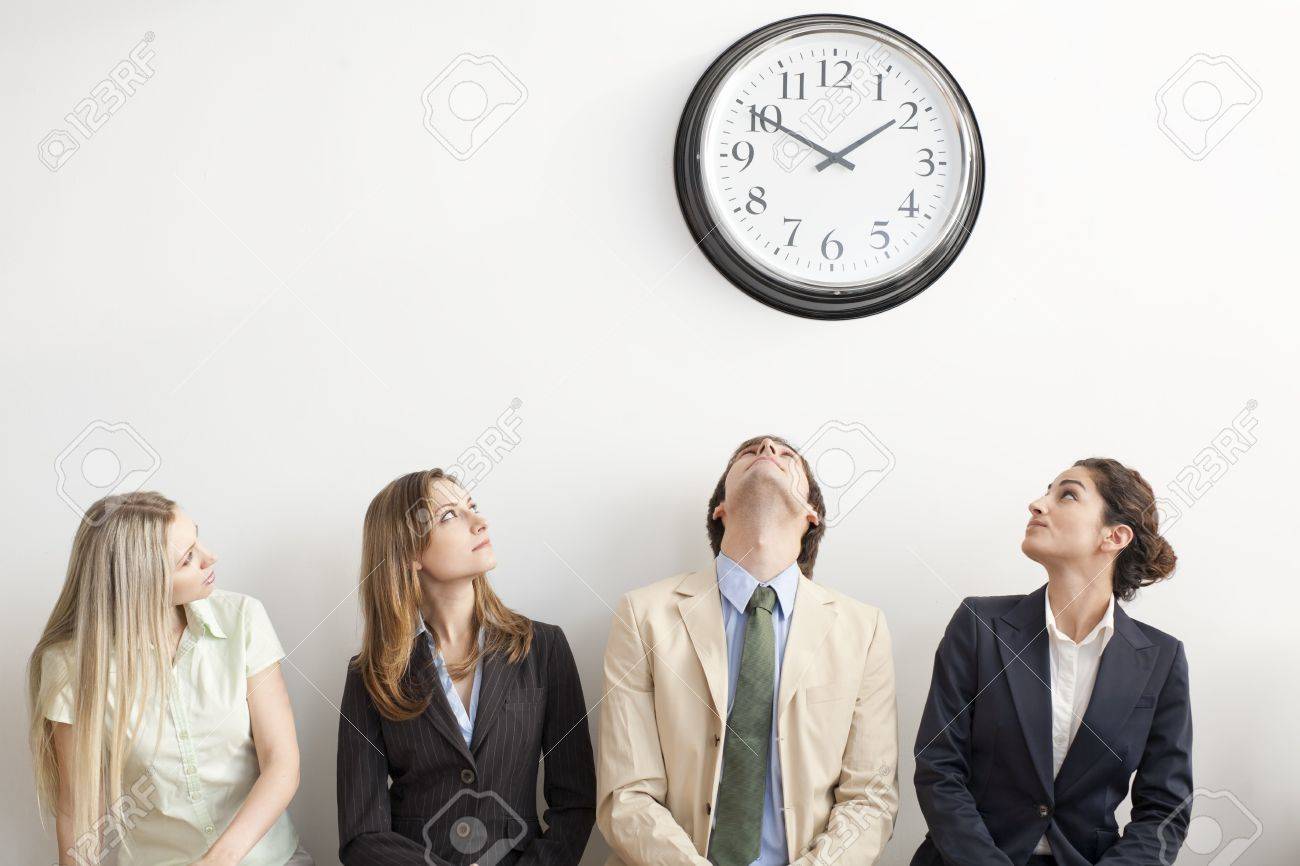 four businesspersons sitting on bench looking up at clock