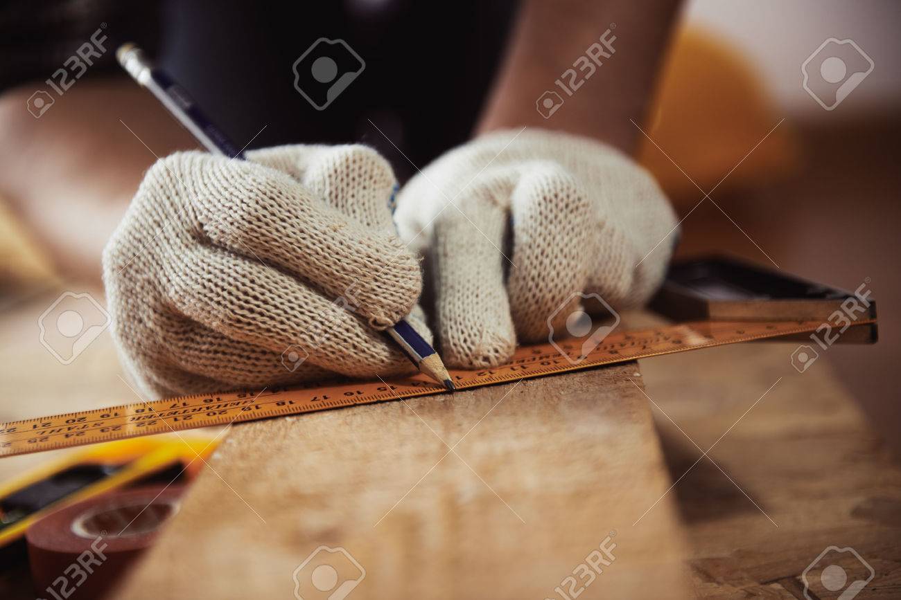Construction work. Woodwork. Male builder marking point on plank sitting on the floor. - 55392563 Construction work. Woodwork. Male builder marking point on plank sitting on the floor. - 55392563
