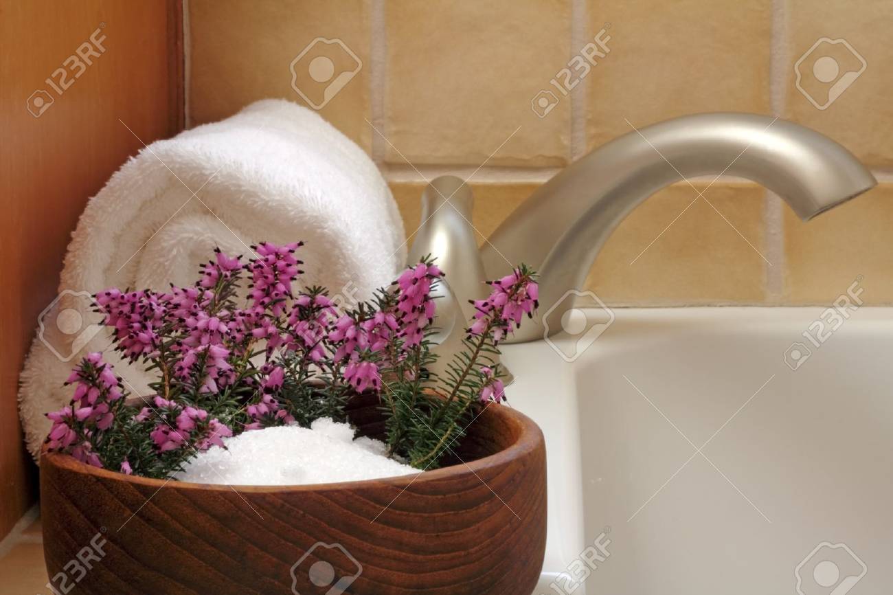Epsom salts in a teak wood bowl with purple heather flowers and white bath towel on edge of a modern bath tub. - 8994809 Epsom salts in a teak wood bowl with purple heather flowers and white bath towel on edge of a modern bath tub. - 8994809