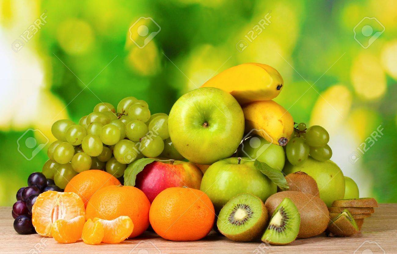 ripe juicy fruits on wooden table on green background stock photo