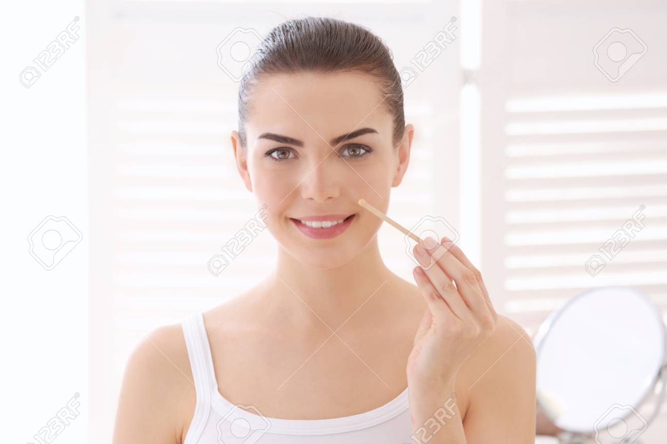 Young Woman Removing Facial Hair With Wax On Blurred Background