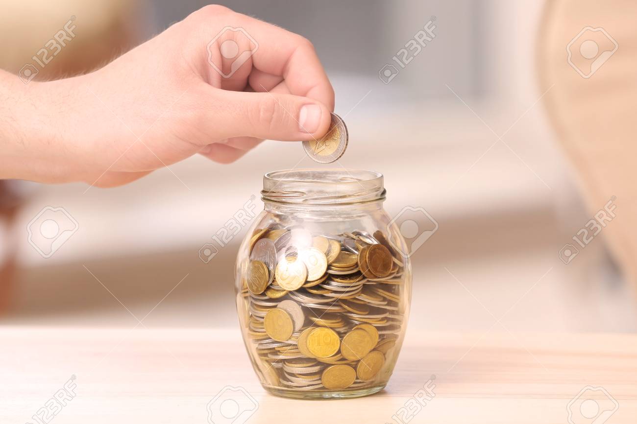 https://previews.123rf.com/images/serezniy/serezniy1812/serezniy181236607/113845487-man-putting-coins-into-glass-jar-on-table-savings-concept.jpg