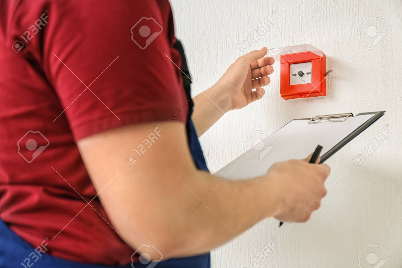 Worker with clipboard near modern fire call point on wall - 114007949 Worker with clipboard near modern fire call point on wall - 114007949
