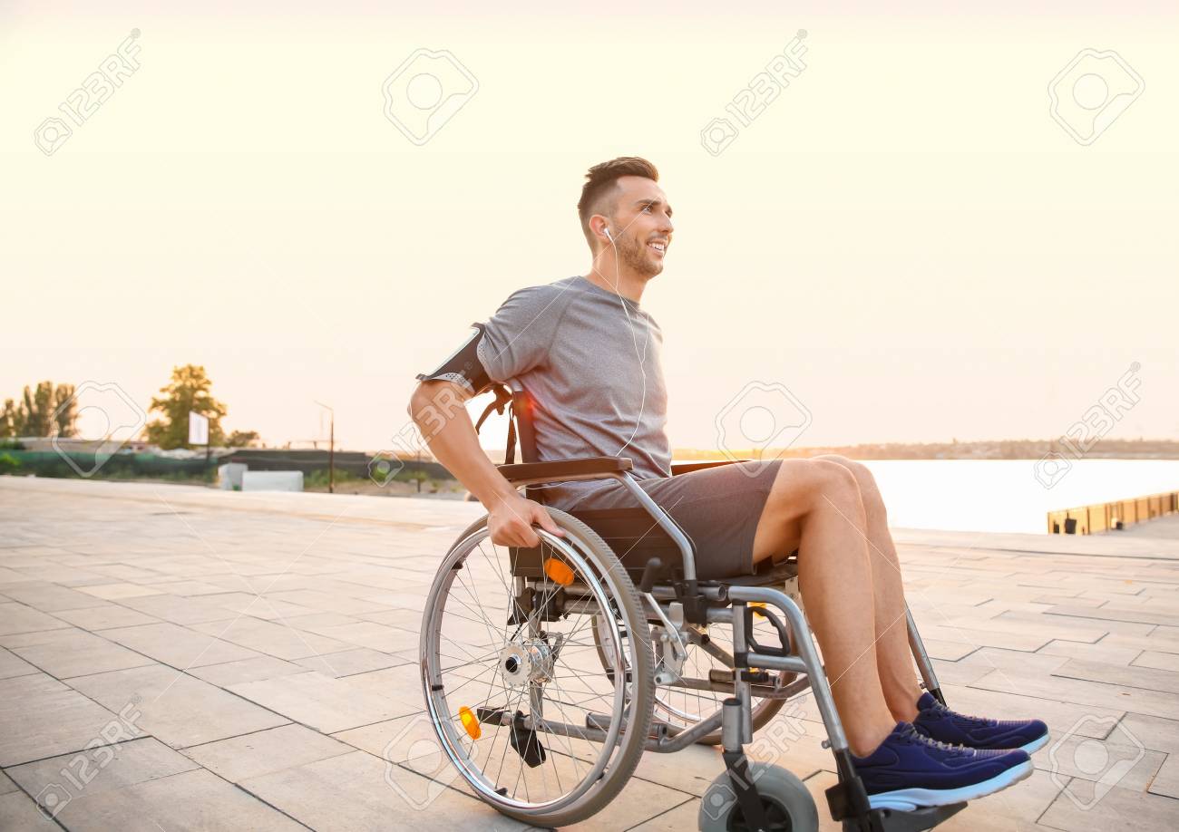 Young man in wheelchair listening to music outdoors - 119746590 Young man in wheelchair listening to music outdoors - 119746590