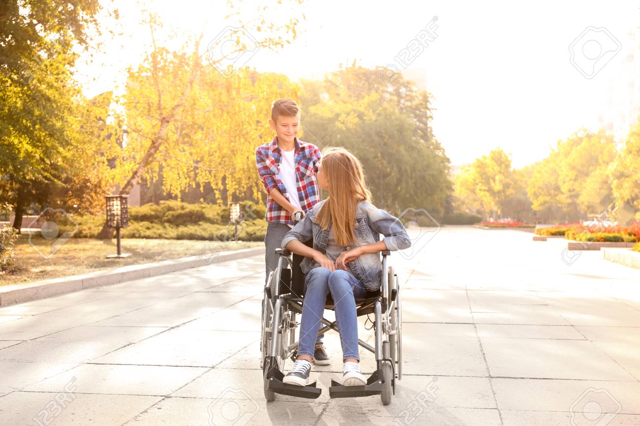 Teenage girl in wheelchair and her brother outdoors - 119754077 Teenage girl in wheelchair and her brother outdoors - 119754077