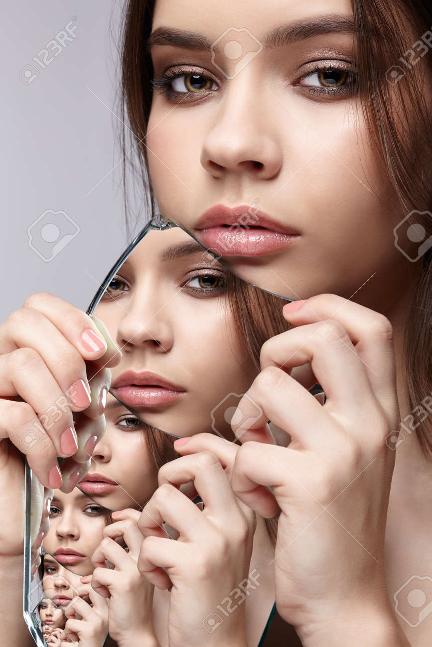 Girl with a shard of the mirror. Female with mirror shard in hand posing on gray background. Multiple reflections in mirror splinter. - 140336520 Girl with a shard of the mirror. Female with mirror shard in hand posing on gray background. Multiple reflections in mirror splinter. - 140336520