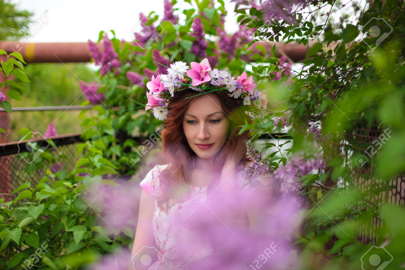 Banque d\u0027images , Belle femme dans une couronne de fleurs près de l\u0027arbre lilas en fleurs. Cheveux rouges, les lèvres.