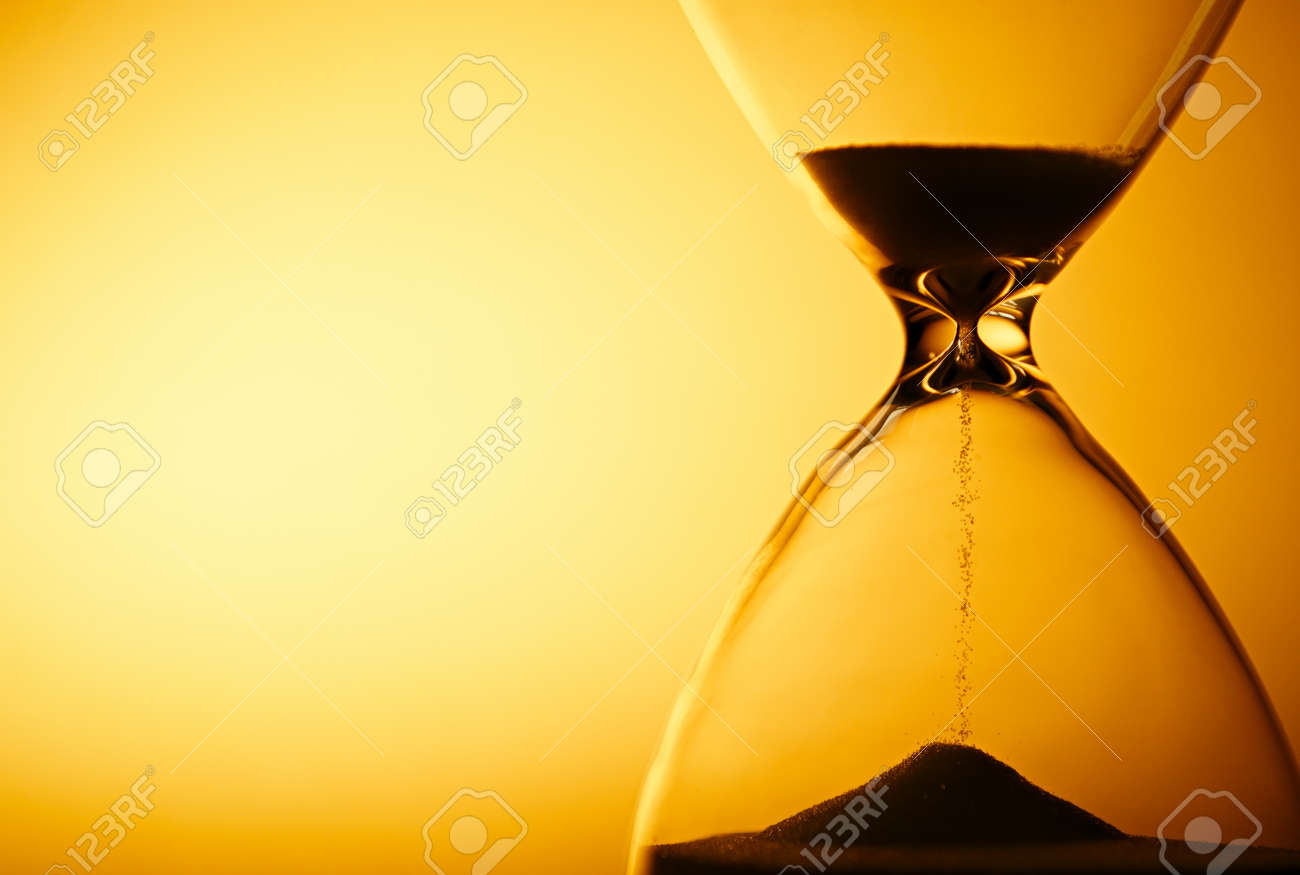 Sand passing through the glass bulbs of an hourglass measuring the passing time as it counts down to a deadline or closure on a yellow background with copyspace - 30765483 Sand passing through the glass bulbs of an hourglass measuring the passing time as it counts down to a deadline or closure on a yellow background with copyspace - 30765483