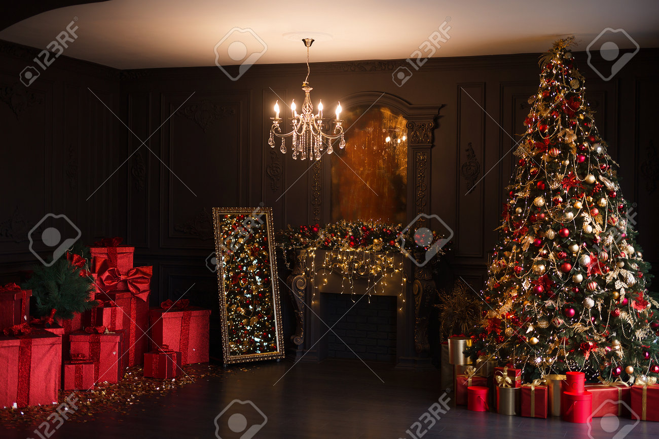 Interior of luxury dark living room with fireplace and chandelier decorated with Christmas tree and gifts - 160565958 Interior of luxury dark living room with fireplace and chandelier decorated with Christmas tree and gifts - 160565958