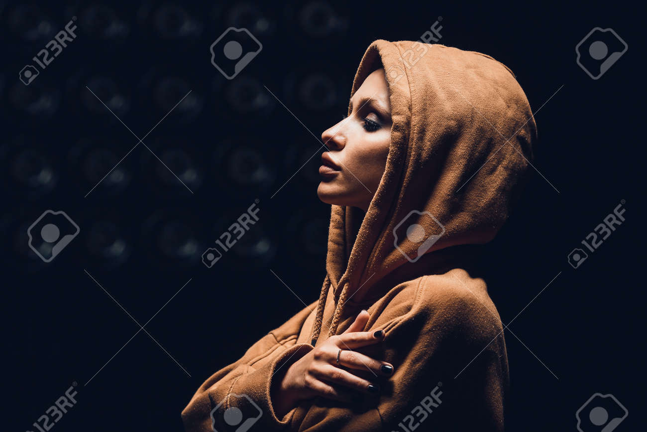 Studio portrait of a girl in a hoodie on a dark background - 165104330 Studio portrait of a girl in a hoodie on a dark background - 165104330
