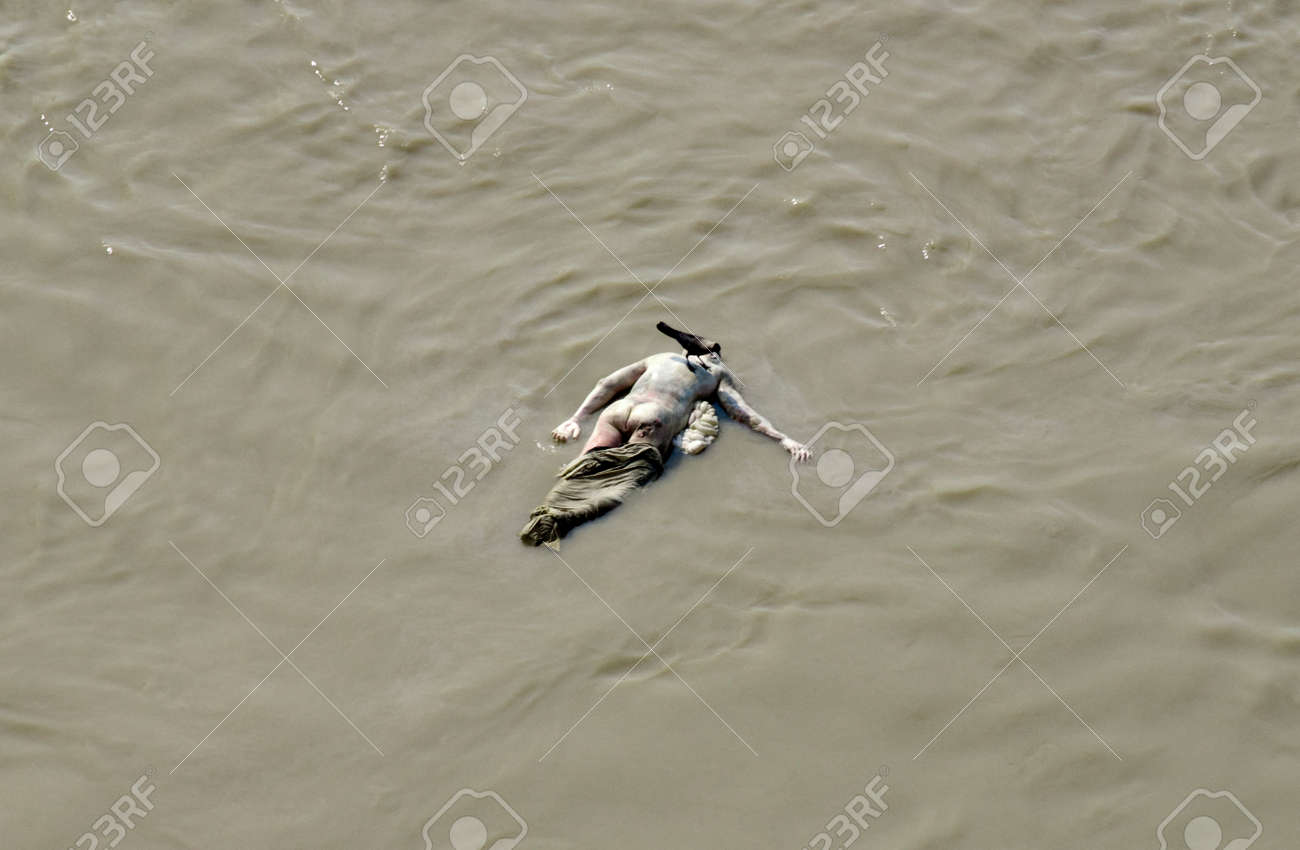 ガンジス川で死に漂っています バラナシ オレンジ色の水平方向のビューには ガンジス川に浮かぶ死体が包まれています バラナシは最高のガートで知られて 川沿いの構造物の 100 以上です ガーツ山脈のほとんどは神聖な B のために使用されます の写真素材 画像素材