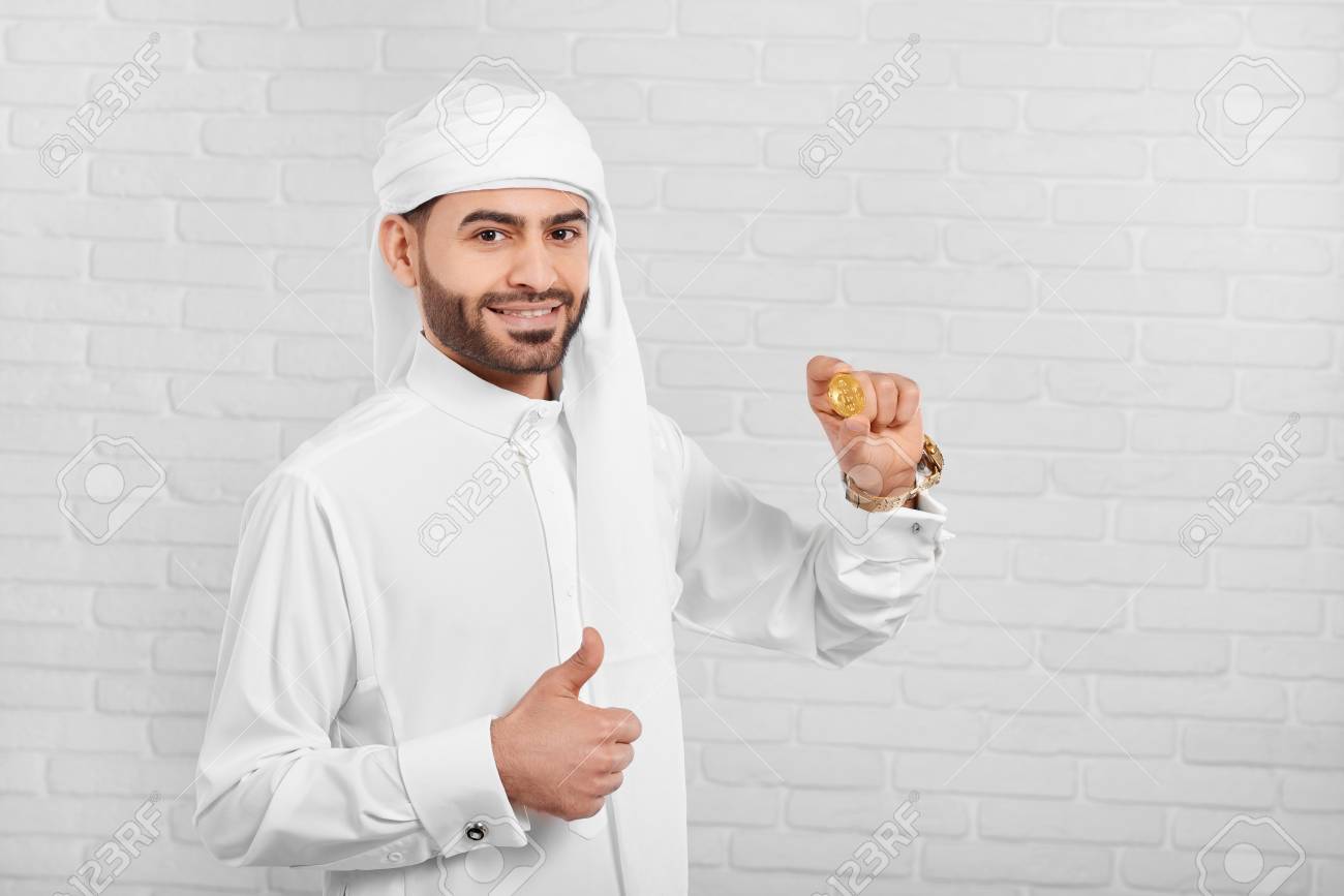 Smiling Arabian Man Keeps Bitcoin And Looks Very Happy. He Wears  Traditional White Arabian Costume,golden Watch And Cufflinks. A Businessman  Looks Very Positive And Happy. Stock Photo, Picture and Royalty Free Image.