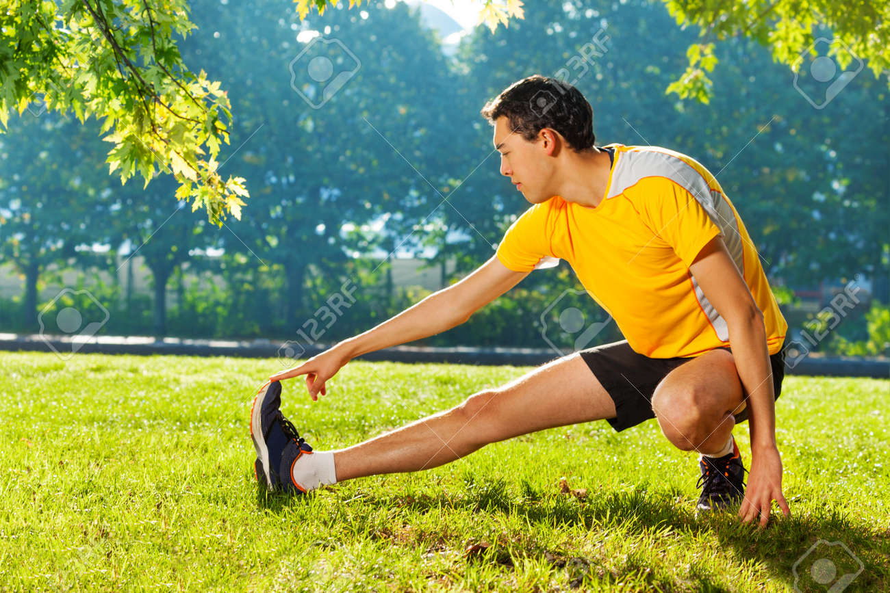 Flexible young man stretching legs outdoors - 98124468 Flexible young man stretching legs outdoors - 98124468