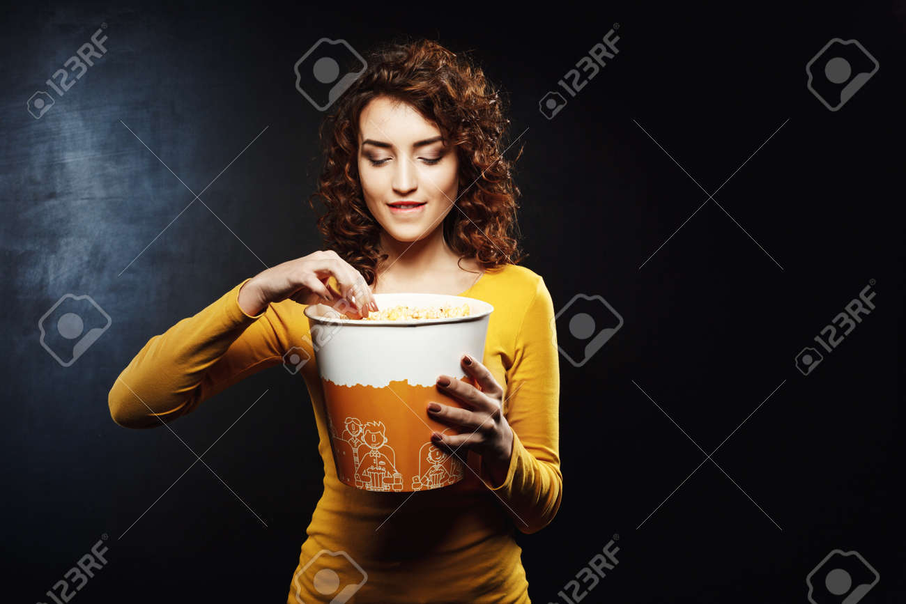 woman with curly hair takes some popcorn biting her underlip stock