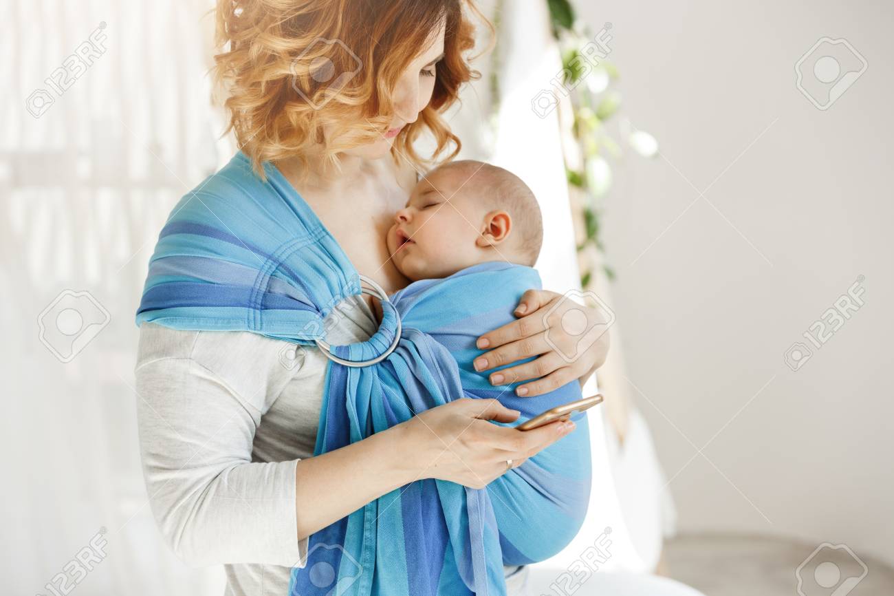 Petit Garcon Qui Dort Tres Fort Avec La Bouche Ouverte Et L Expression Du Visage Doux Dans Une Echarpe Pendant Que Maman Se Repose En Lisant Les Nouvelles Du Monde Au Telephone Concept