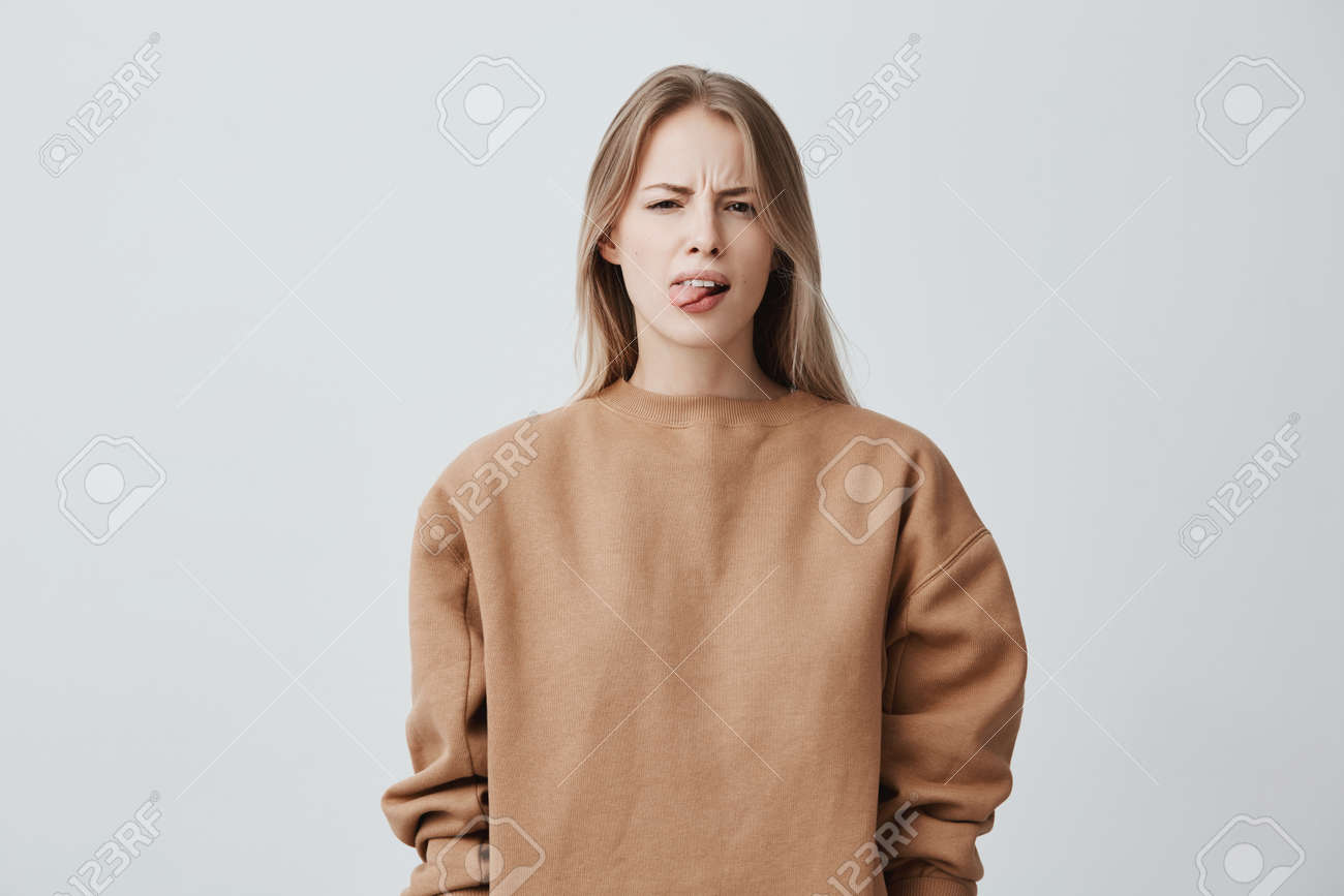 Naughty Beautiful Girl With Blonde Long Hair In Beige Sweater Misbehaving Sticking Out Tongue At Naughty Beautiful Girl With Blonde Long Hair In Beige Sweater Misbehaving Sticking Out Tongue At