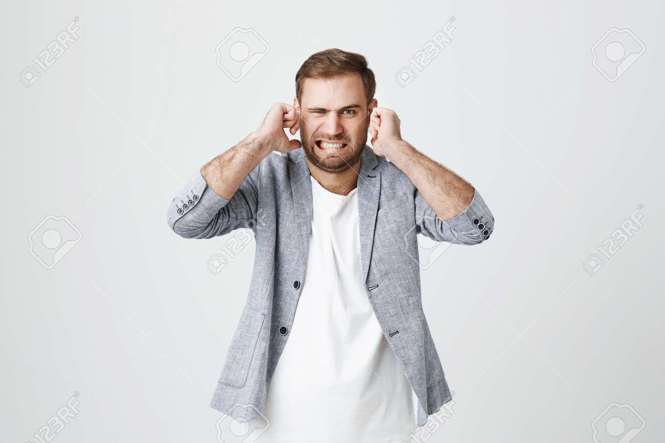 Irritated handsome bearded male with displeased facie expression, plugs ears, clenches teeth, expresses negativeness, avoids noise, isolated against gray background. Stop this annoying sound! - 94288488 Irritated handsome bearded male with displeased facie expression, plugs ears, clenches teeth, expresses negativeness, avoids noise, isolated against gray background. Stop this annoying sound! - 94288488