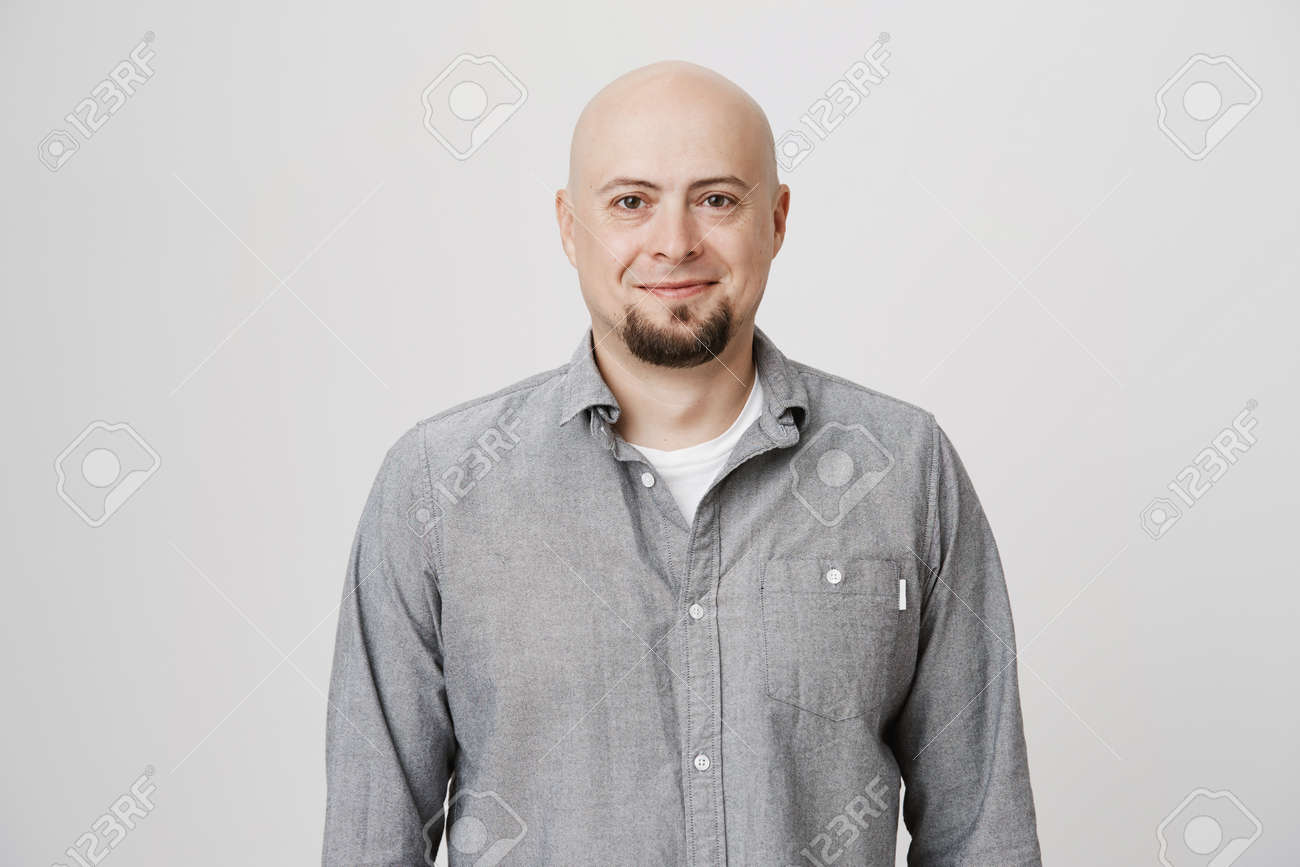 人間の顔の表情や感情 カジュアルな服を着た思慮深い格好のハゲ男は カメラを見て 楽しそうに微笑んでいます 屋内でポーズ毛のないポジティブな男性モデル の写真素材 画像素材 Image