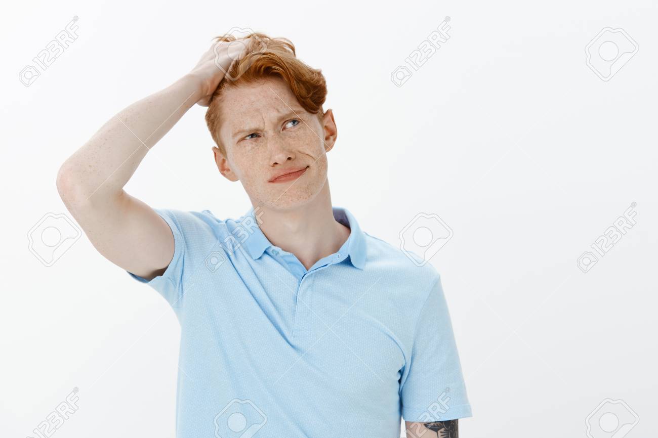 Guy Has Problems With Making Decisions Confused Unaware Handsome Redhead Man And Freckles Looking Up And Smirking Touching Hair While Thinking Or Making Choice Hesitating Over Grey Wall Stock Photo Picture And