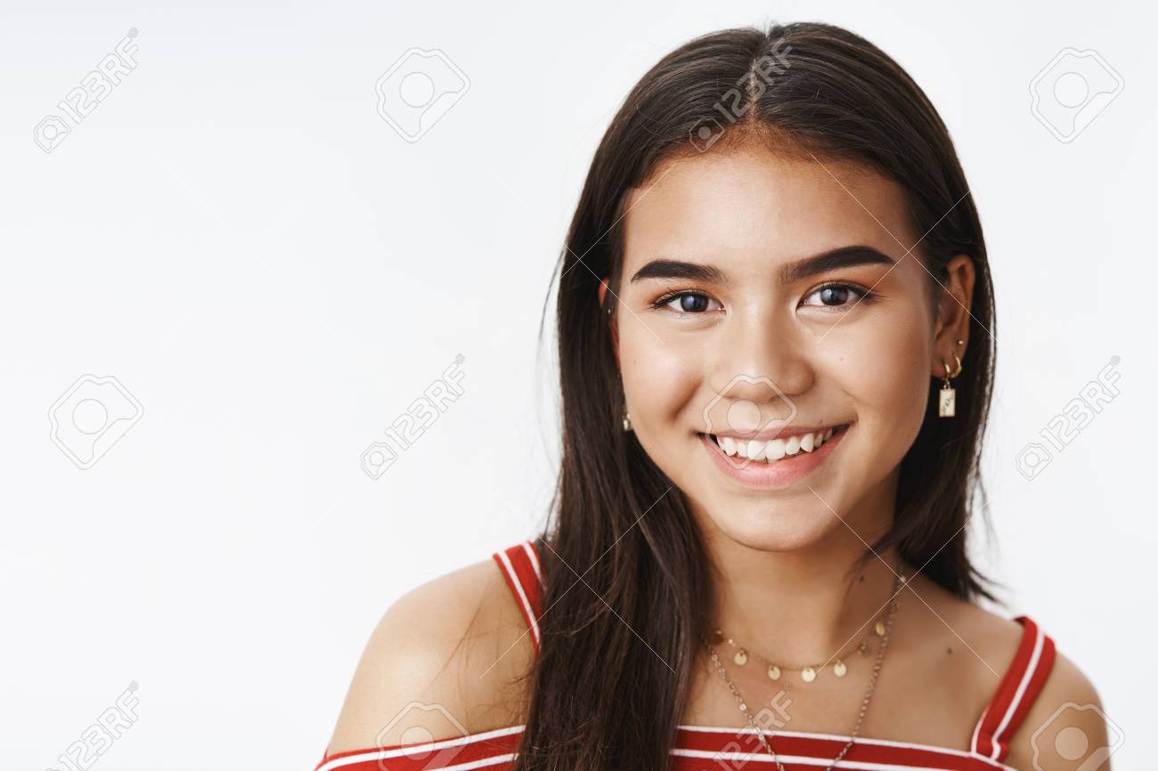 Studio Shot Of Good-looking Indian Teenage Girl In Blouse And Earrings  Smiling Joyfully And Gazing At Camera Friendly And Kind Over Gray  Background, Talking With Friends At School Over Gray Wall Stock, image size:1300x866