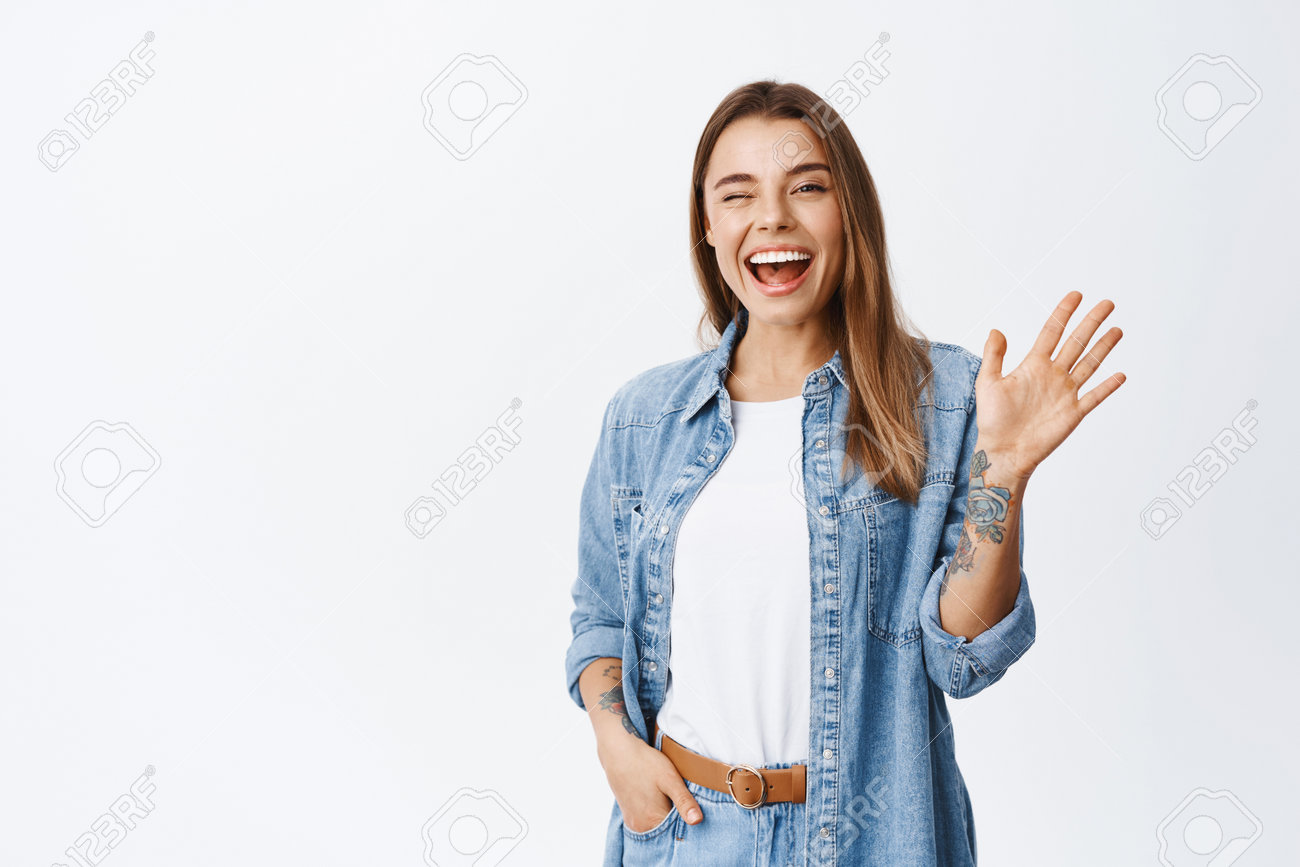 Cheerful Friendly Girl Saying Hello, Winking And Smiling, Waving Hand At  Camera, Say Hi And Greet You, Standing Against White Background Stock  Photo, Picture and Royalty Free Image. Image 165369804., image size:1300x867