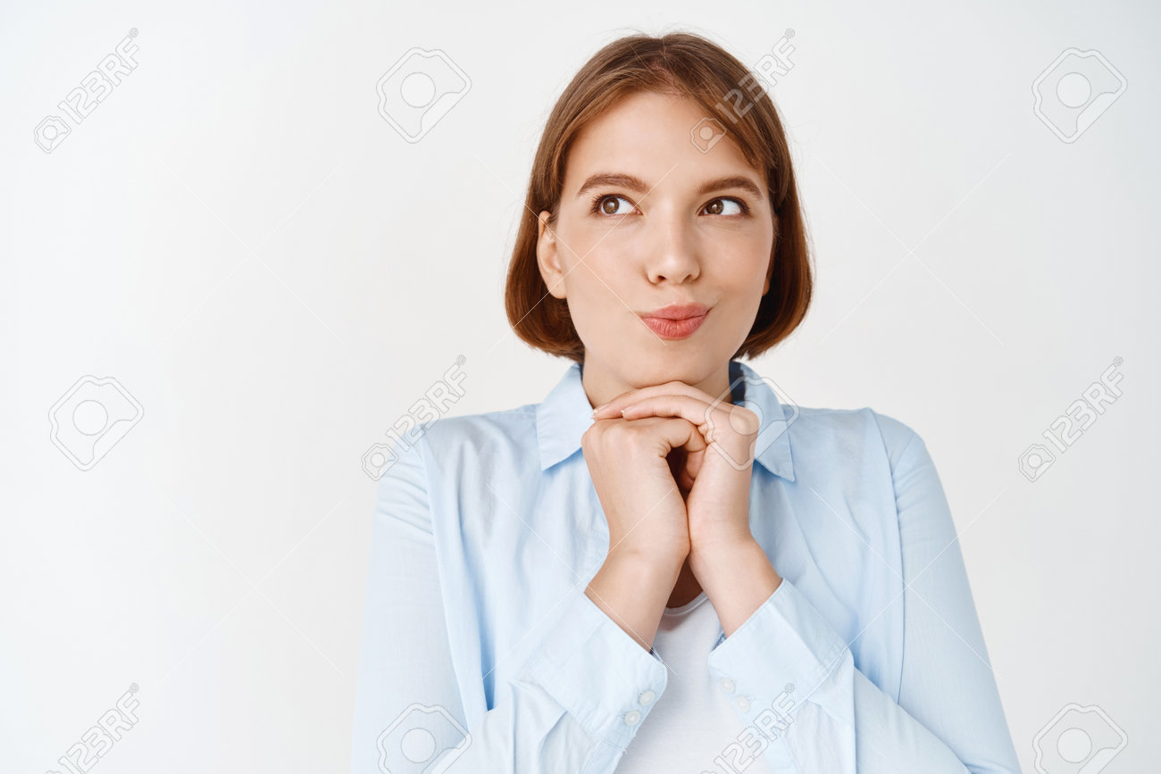 うーん、考えさせてください。夢のような思いやりのある女の子が物事をイメージし、尖塔の指と興味をそそる顔で脇を見て、白い背景のブラウスに立っていますの写真素材・画像素材  Image 165515728