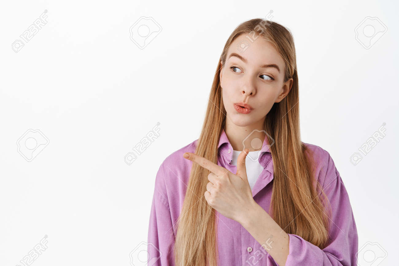 若い女の子の画像は脇に好奇心をそそる、思慮深い興味をそそる顔で広告を左に向けて見つめ、何かをチェックし、白い背景の上に立っているように見えますの写真素材・画像素材  Image 168346053