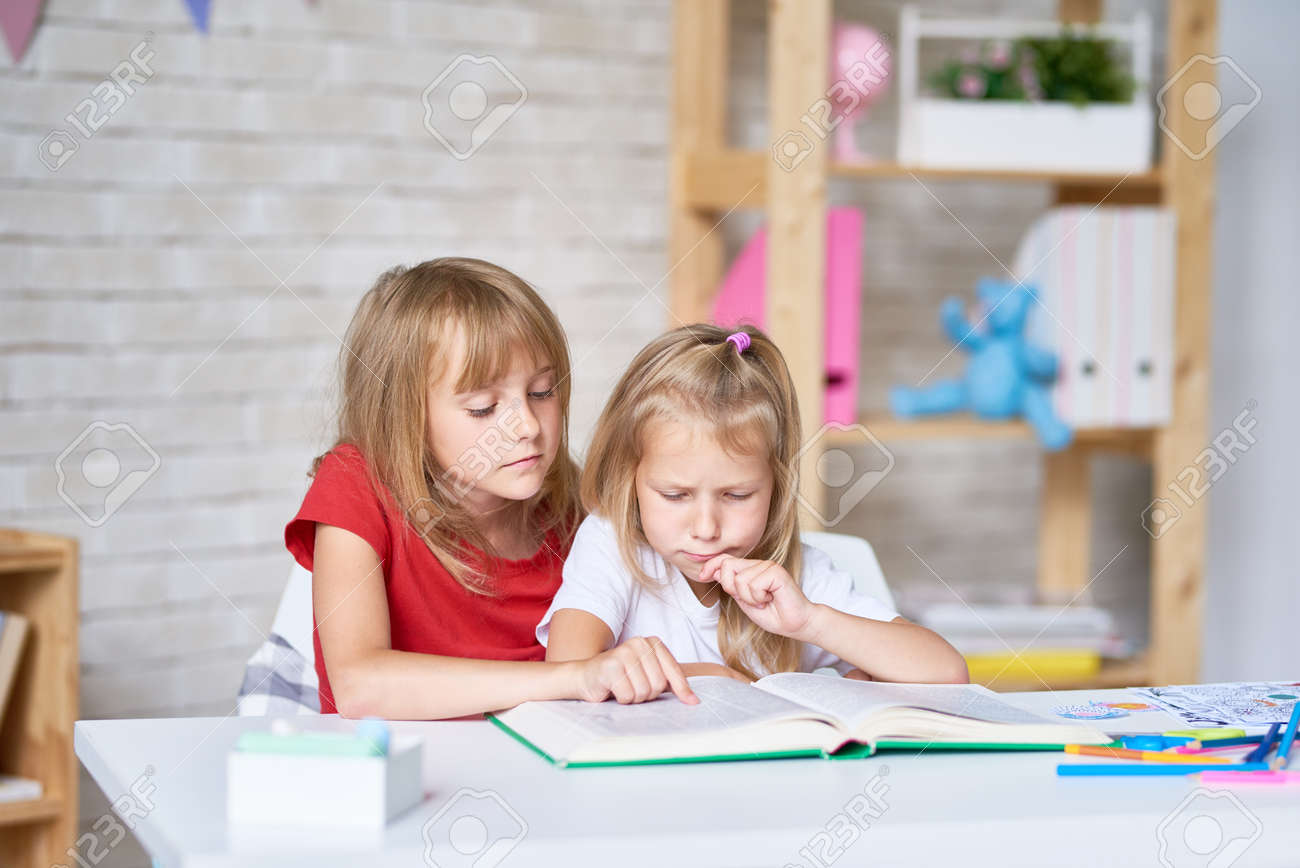 Adorable little sisters wrapped up in reading adventure story while sitting at table in their cozy bedroom - 83829592 Adorable little sisters wrapped up in reading adventure story while sitting at table in their cozy bedroom - 83829592