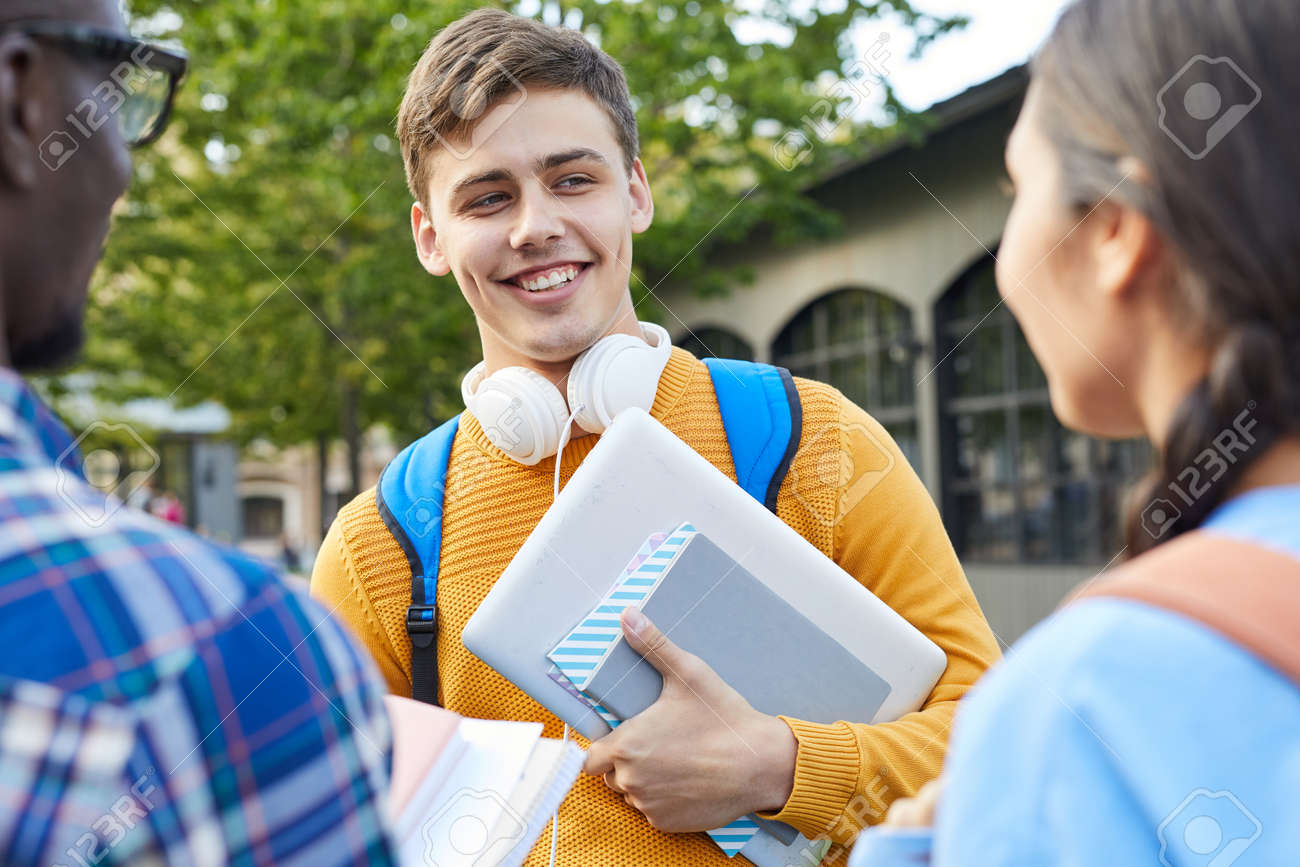 Waist up portrait of cheerful college student talking to friends outdoors in campus, copy space - 128446454 Waist up portrait of cheerful college student talking to friends outdoors in campus, copy space - 128446454