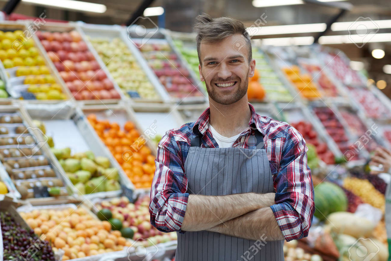 Waist up portrait of handsome young man working in supermarket and smiling at camera while posing by fruit stand, copy space - 128446655 Waist up portrait of handsome young man working in supermarket and smiling at camera while posing by fruit stand, copy space - 128446655