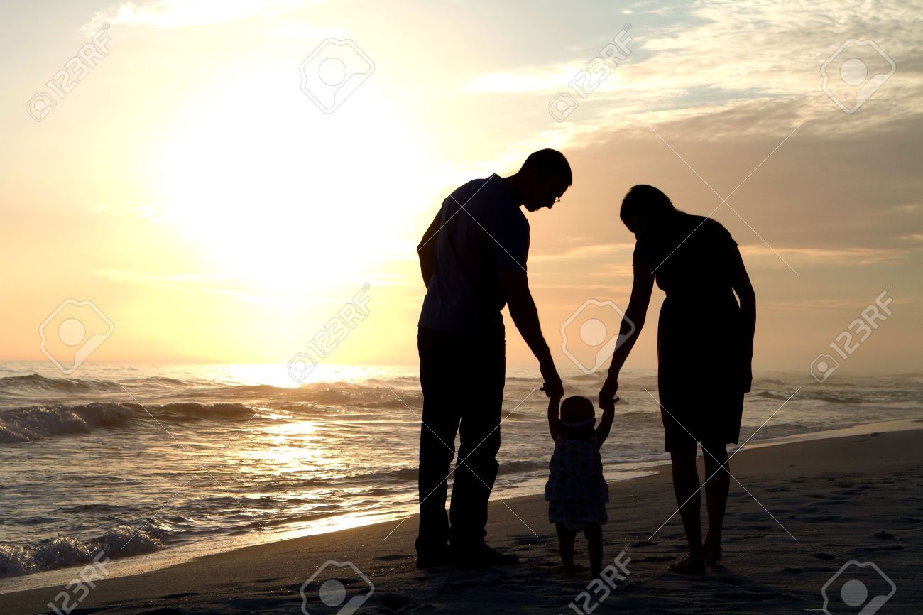 Hombre Y Mujer Padres De Un Nino De Corta Edad A Pie A Su Bebe Por La Playa Tomados De La Mano En La Arena Cerca De La Puesta Del Sol Como Hombre Y Mujer Padres De Un Nino De Corta Edad A Pie A Su Bebe Por La Playa Tomados De La Mano En La Arena Cerca De La Puesta Del Sol Como