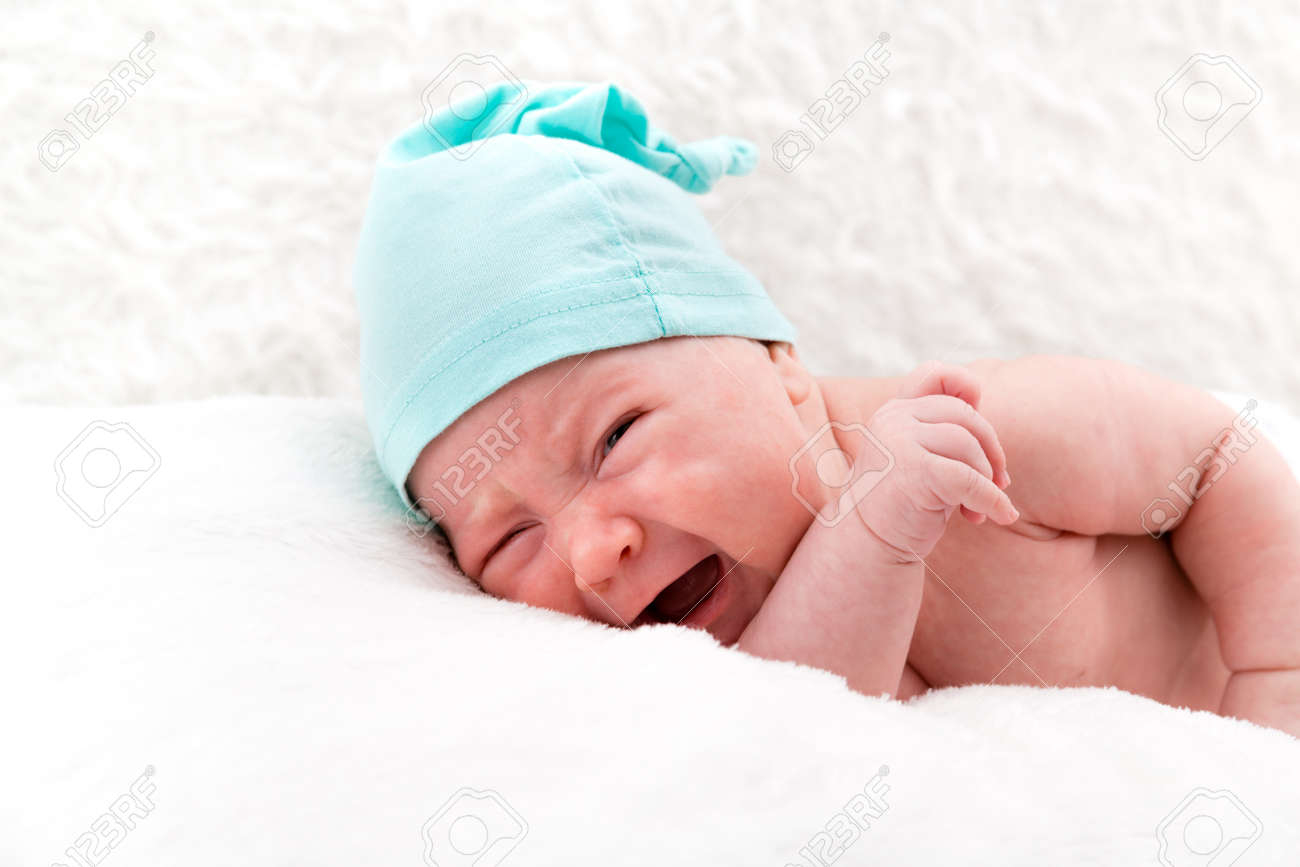 Crying newborn baby without clothes and in a cap on white pillows. - 124791655 Crying newborn baby without clothes and in a cap on white pillows. - 124791655