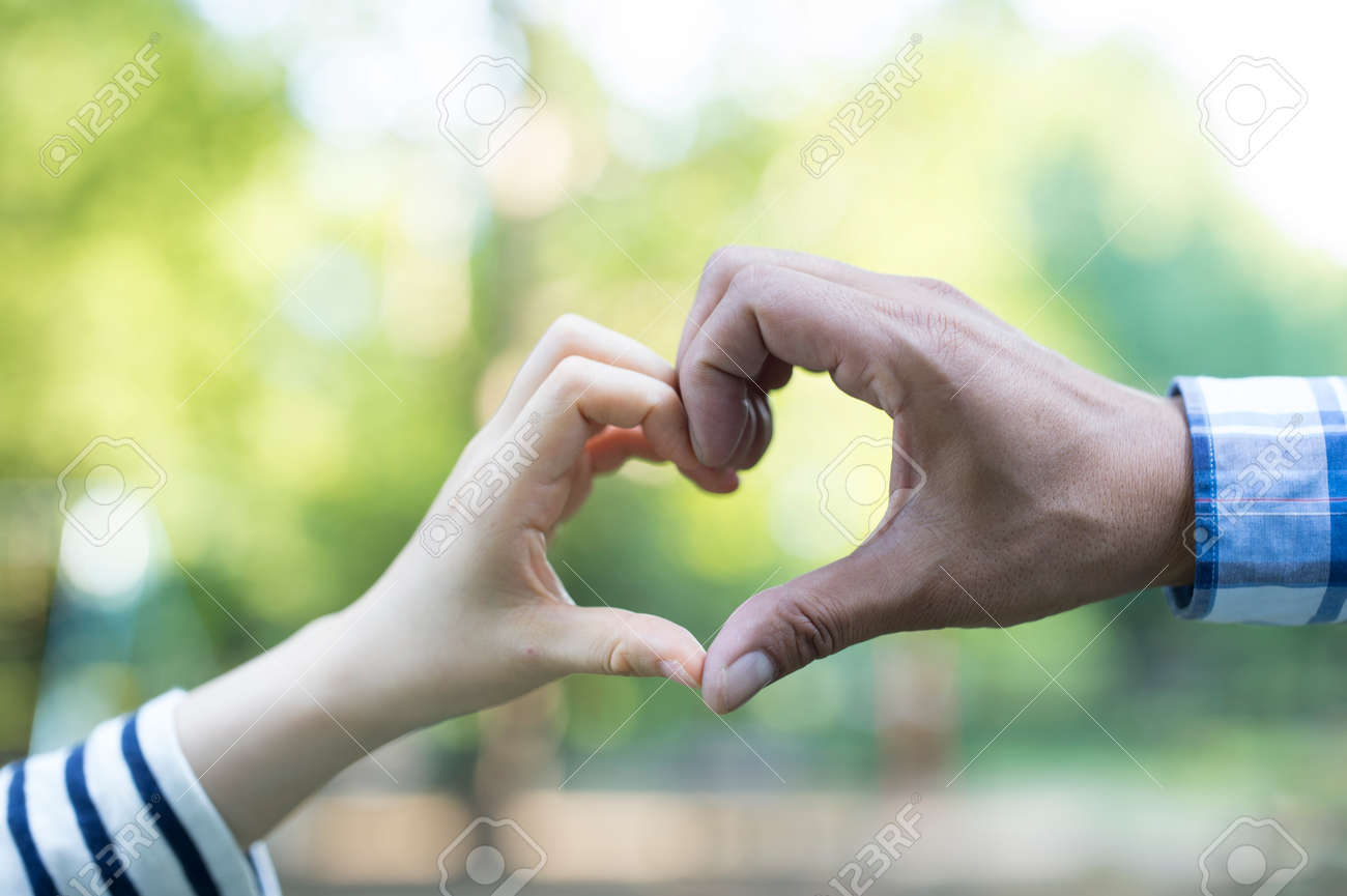 shiloutte of two hands join to form a heart shape with sun beam photography form