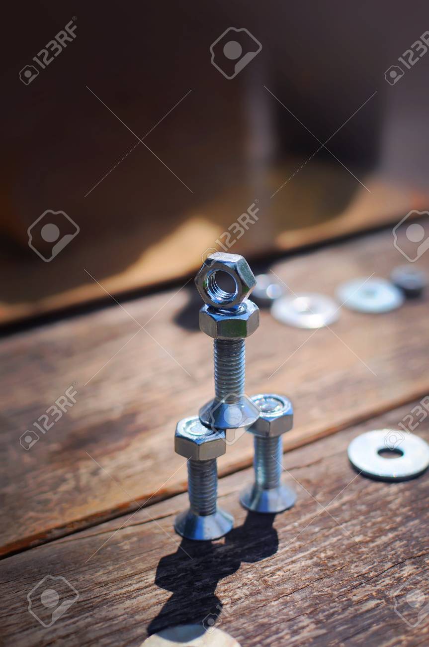 Una Figura De Un Pequeño Robot Montado A Partir De Pernos Y Tuercas De Pie Posición Vertical Una Mesa Hecha De Tablas. Simboliza Tecnología, Progreso, Ingeniería E Industrialización Fotos,