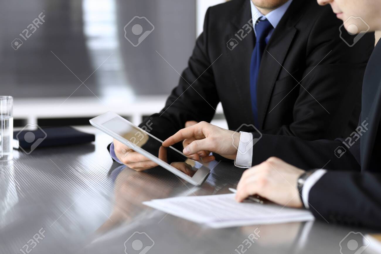 Businessman using tablet computer and work together with his colleague or partner at the glass desk in modern office, close-up. Unknown business people at meeting. Teamwork and partnership concept. - 133114011 Businessman using tablet computer and work together with his colleague or partner at the glass desk in modern office, close-up. Unknown business people at meeting. Teamwork and partnership concept. - 133114011