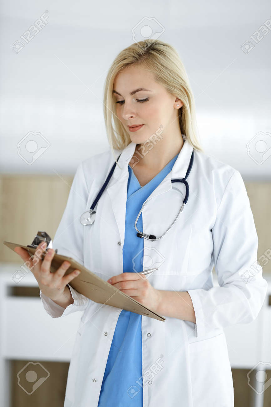 Woman-doctor standing in hospital or clinic and filling up medication history record form. Data and best service in medicine and healthcare - 158220720 Woman-doctor standing in hospital or clinic and filling up medication history record form. Data and best service in medicine and healthcare - 158220720