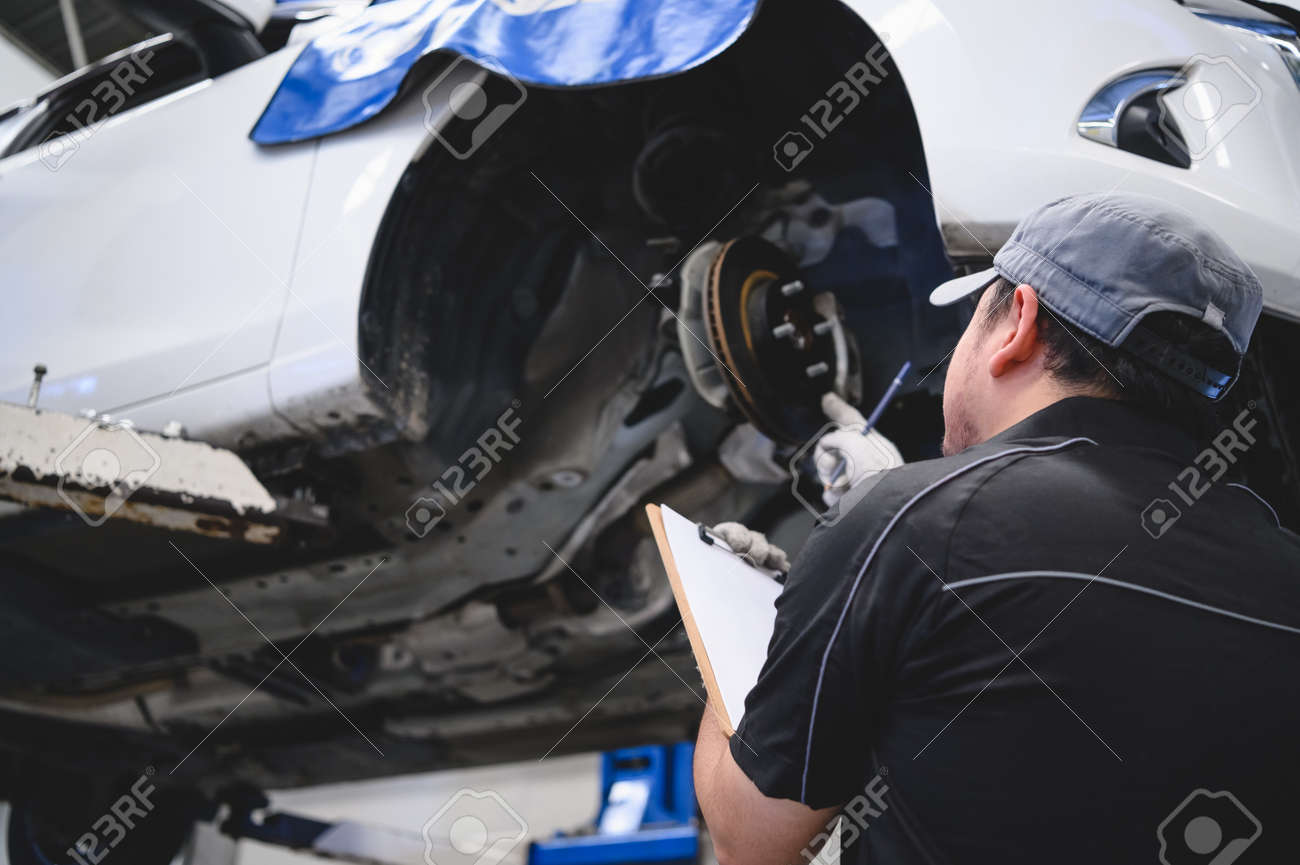 Asian male car technician car maintenance for customers according to specified vehicle maintenance checklist. Disk brake pad wear automotive repairing on vehicle. Safety inspection check service - 129403205 Asian male car technician car maintenance for customers according to specified vehicle maintenance checklist. Disk brake pad wear automotive repairing on vehicle. Safety inspection check service - 129403205