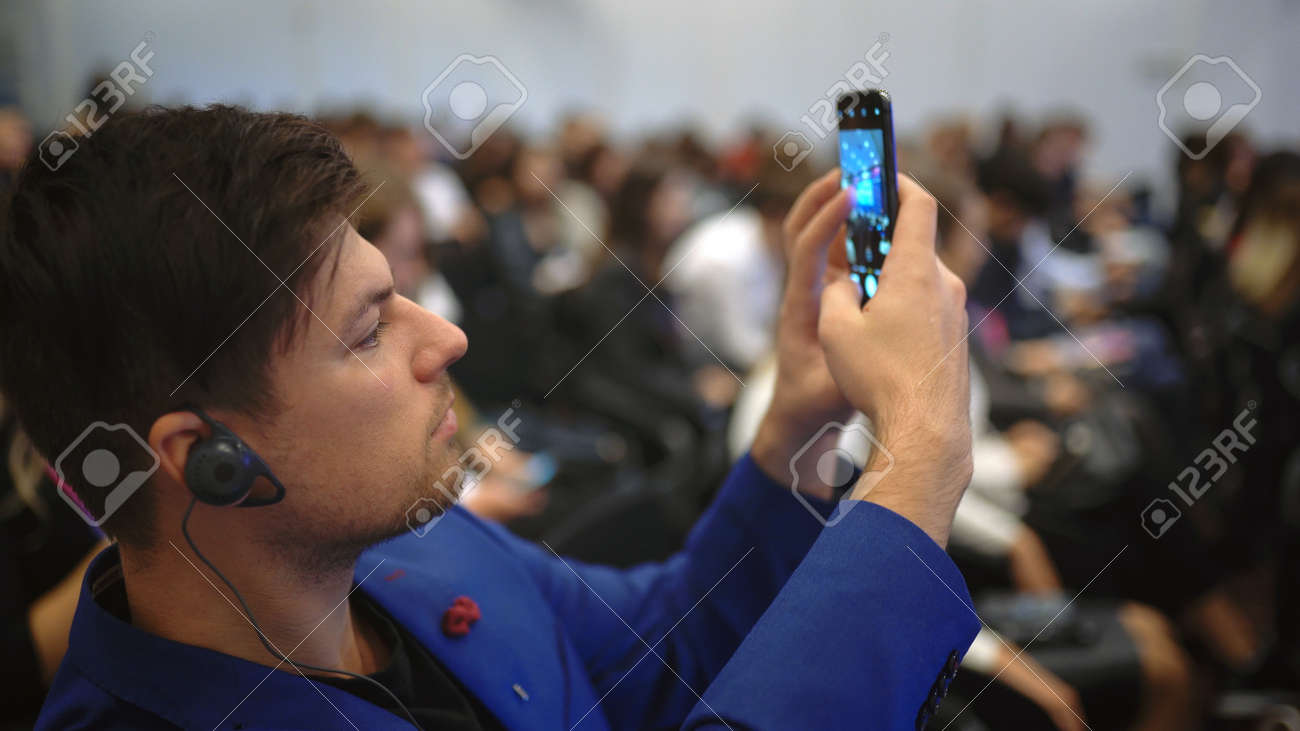 Person take photo on phone in crowded audience business forum. Conference business man with mobile. Seminar for viewer auditorium. group people listen speaker speech. Taking photography scene on phone - 156059684 Person take photo on phone in crowded audience business forum. Conference business man with mobile. Seminar for viewer auditorium. group people listen speaker speech. Taking photography scene on phone - 156059684