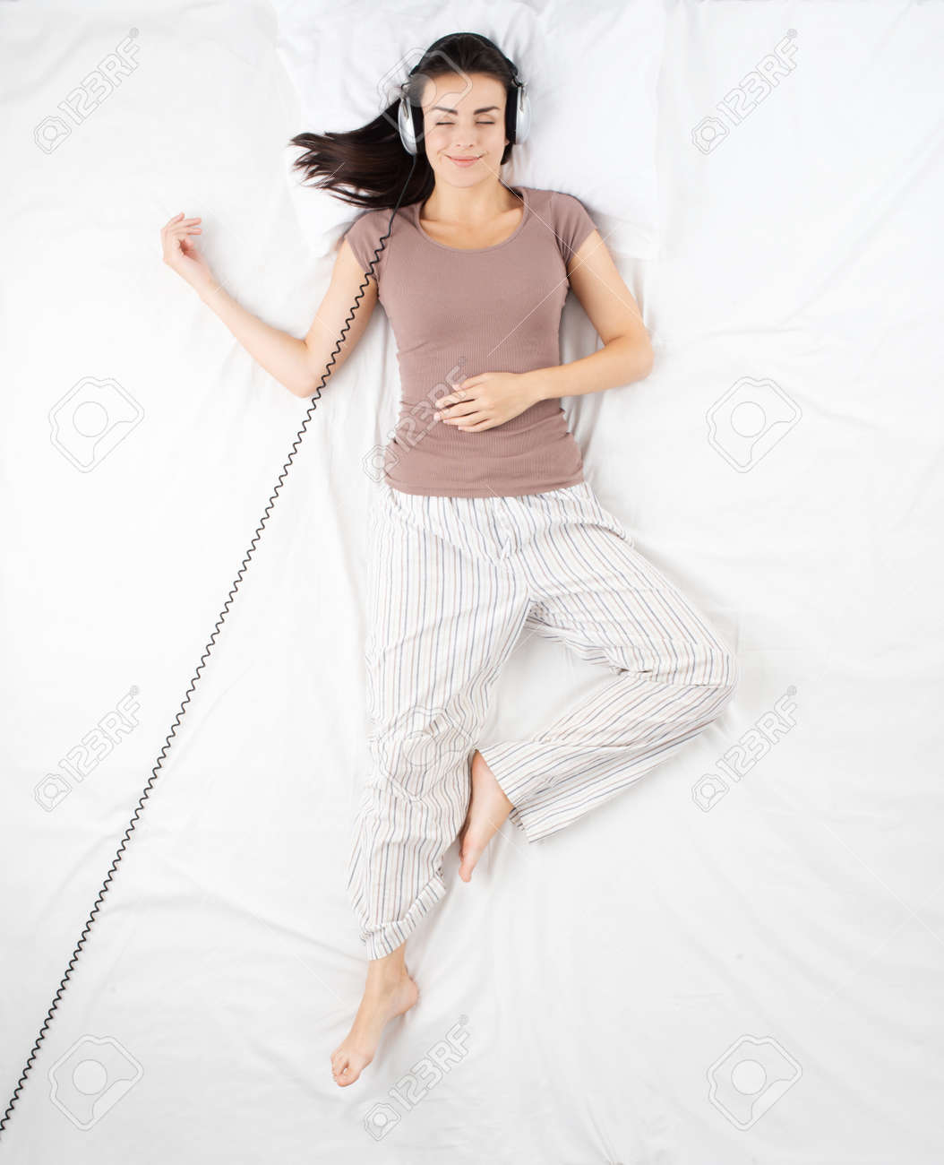 大きなヘッドホンで白いベッドで寝ているかわいい幸せな女 就寝前に音楽を聴く女性 の写真素材 画像素材 Image