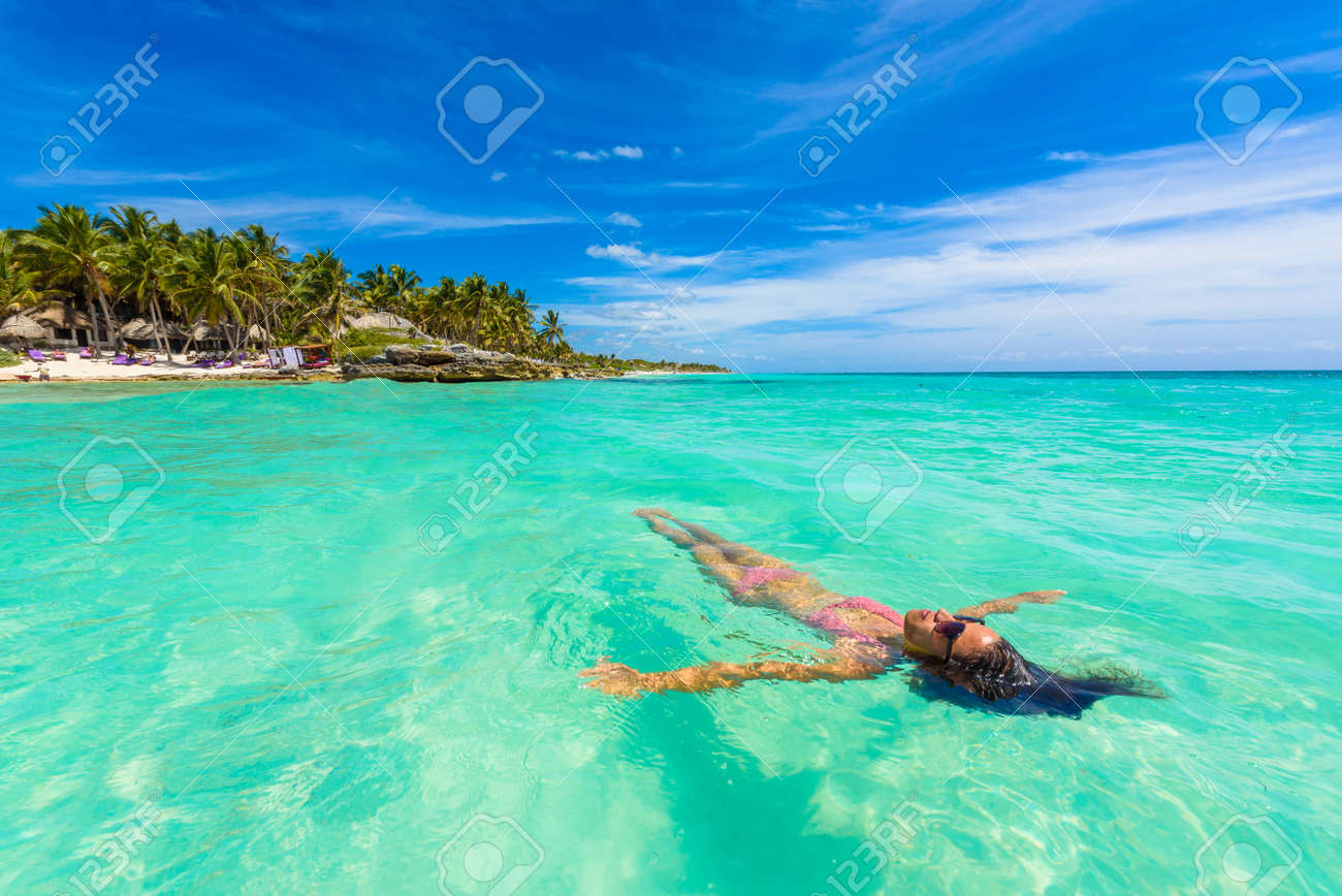 Attractive young woman relaxing in turquoise waters of Caribbean Sea in front of paradise beach in Tulum, close to Cancun, Riviera Maya, Mexico - 97631025 Attractive young woman relaxing in turquoise waters of Caribbean Sea in front of paradise beach in Tulum, close to Cancun, Riviera Maya, Mexico - 97631025
