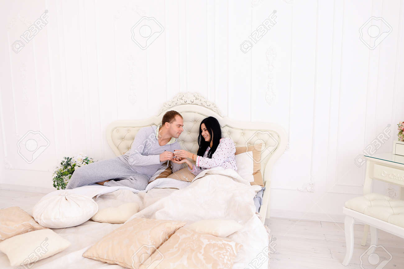 おはようの女の子のベッドにコーヒーを持って思いやりのある男 夫 妻のベッド に座っています お母さん お父さんの欧州外観 幸せな家族生活 エンターテイメント 成功のコンセプトはホテルの広告や家具を寝具 ベッドでの朝食します の写真素材 画像素材 Image
