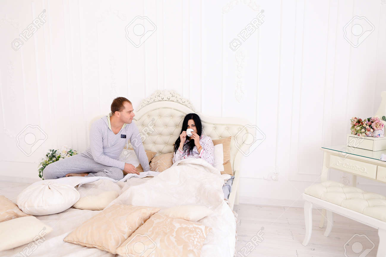 おはようの女の子のベッドにコーヒーを持って思いやりのある男 夫 妻のベッド に座っています お母さん お父さんの欧州外観 幸せな家族生活 エンターテイメント 成功のコンセプトはホテルの広告や家具を寝具 ベッドでの朝食します の写真素材 画像素材 Image
